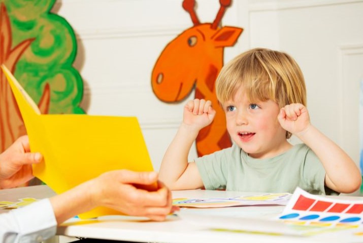 Diagnostic précoce de l'autisme : un jeune enfant serre les poings, les mains levées, tandis que les mains d'une adulte lui montrent une farde jaune
