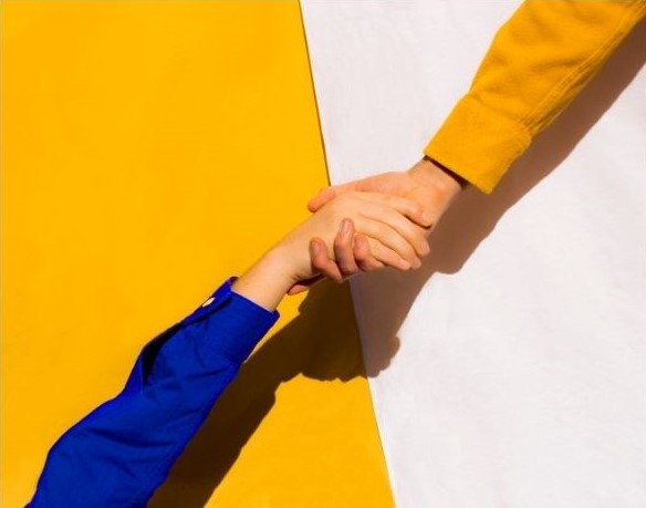 un bras jaune sur fond beige serre un autre bras bleu sur fond jaune en bas