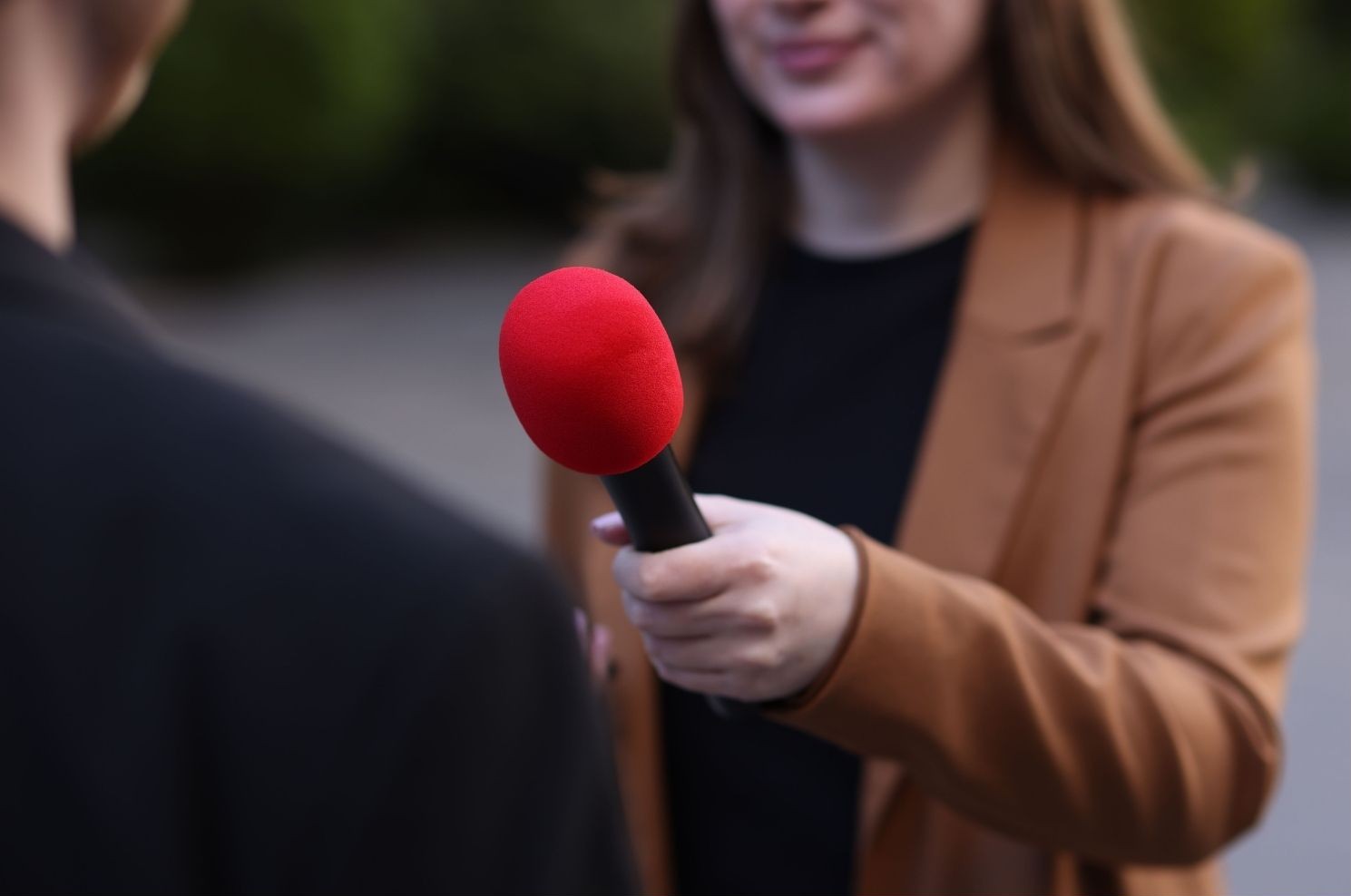 Message de journaliste : une journaliste tient un micro et elle interviewe un homme de dos. On ne voit pas les visages